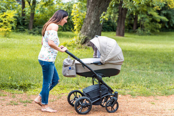 Молодая мать, гуляющая со своим ребенком в коляске в парке Стоковое Фото