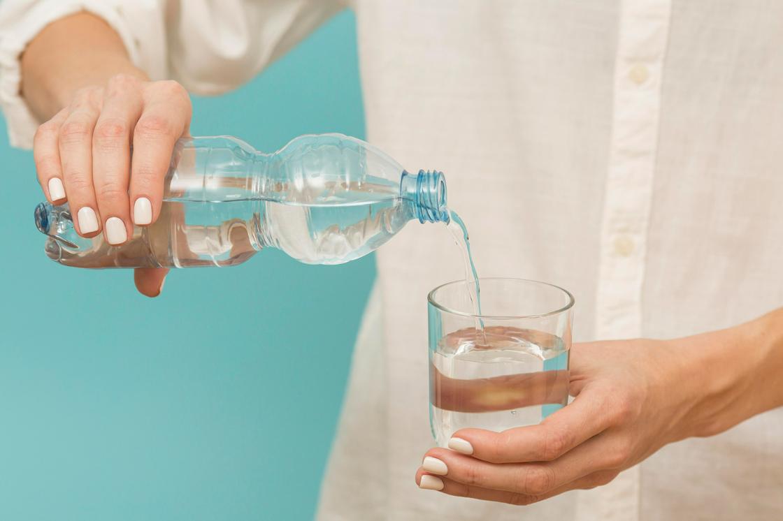 Женщина наливает в стакан минеральную воду из бутылки